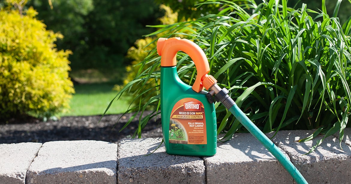 a bottle of weed killer sits on a stone wall. The distinctive, curved handle is connected to a green hose.